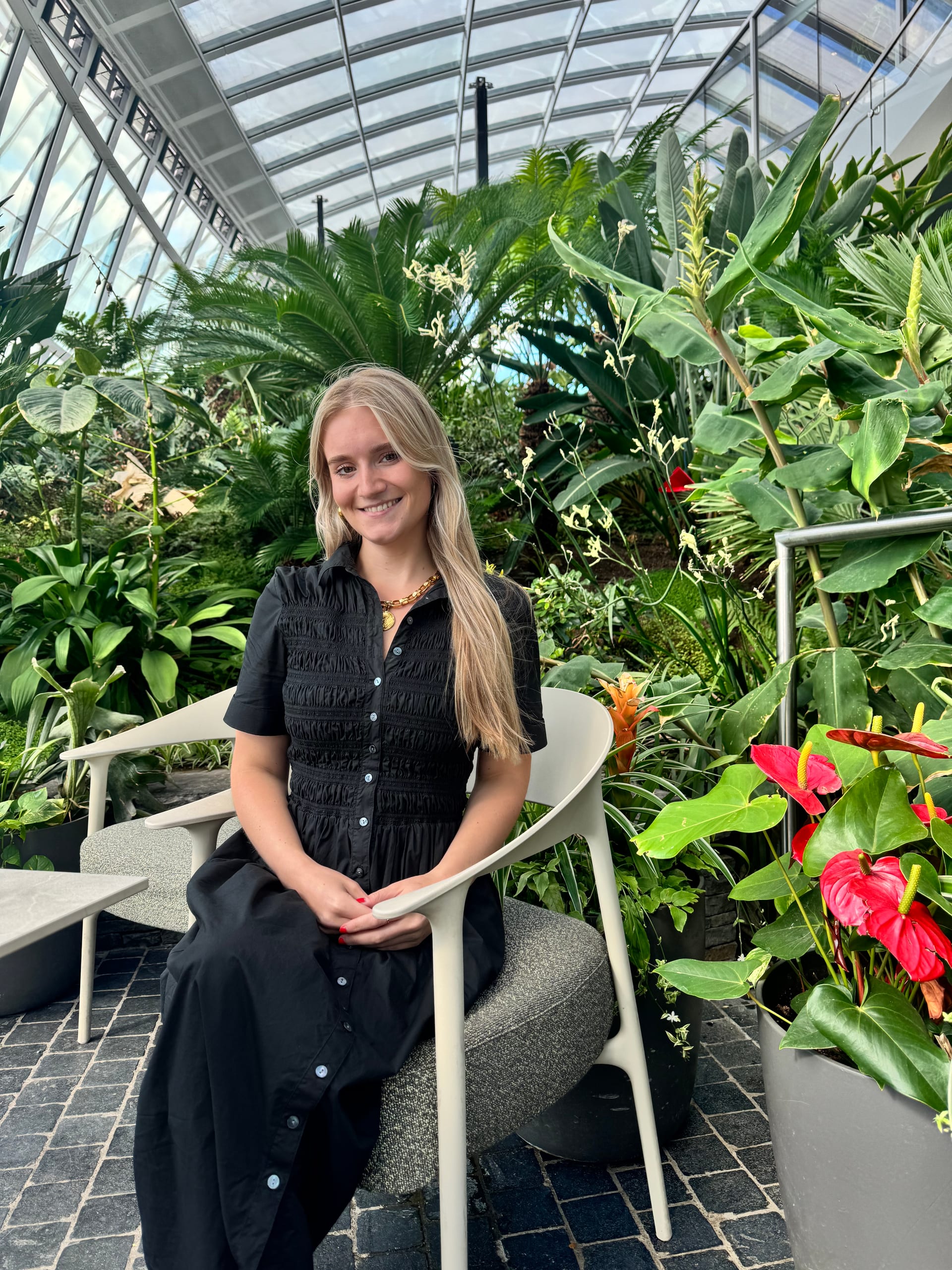 Carson Miller seated in a black dress among tropical plants at the Sky Garden in London.